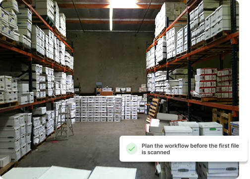 Warehouse interior with tall shelves of stacked boxes and crates, concrete floor.
